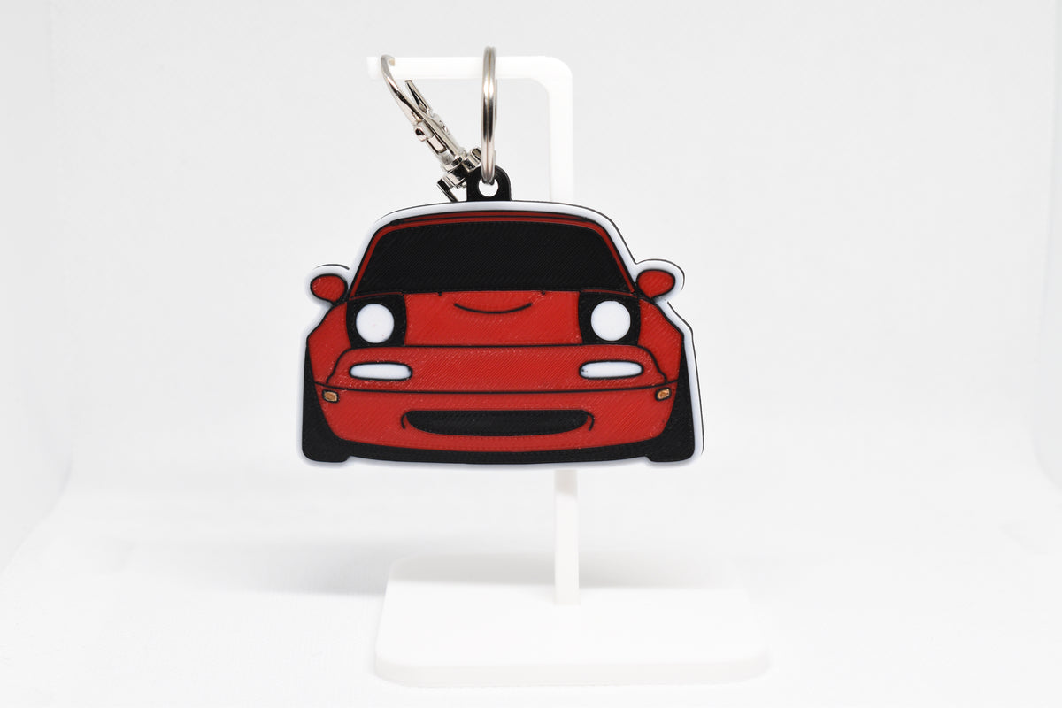 Pocket Motors Mazda Miata NA keychain displayed on a white stand with metal ring and clip.