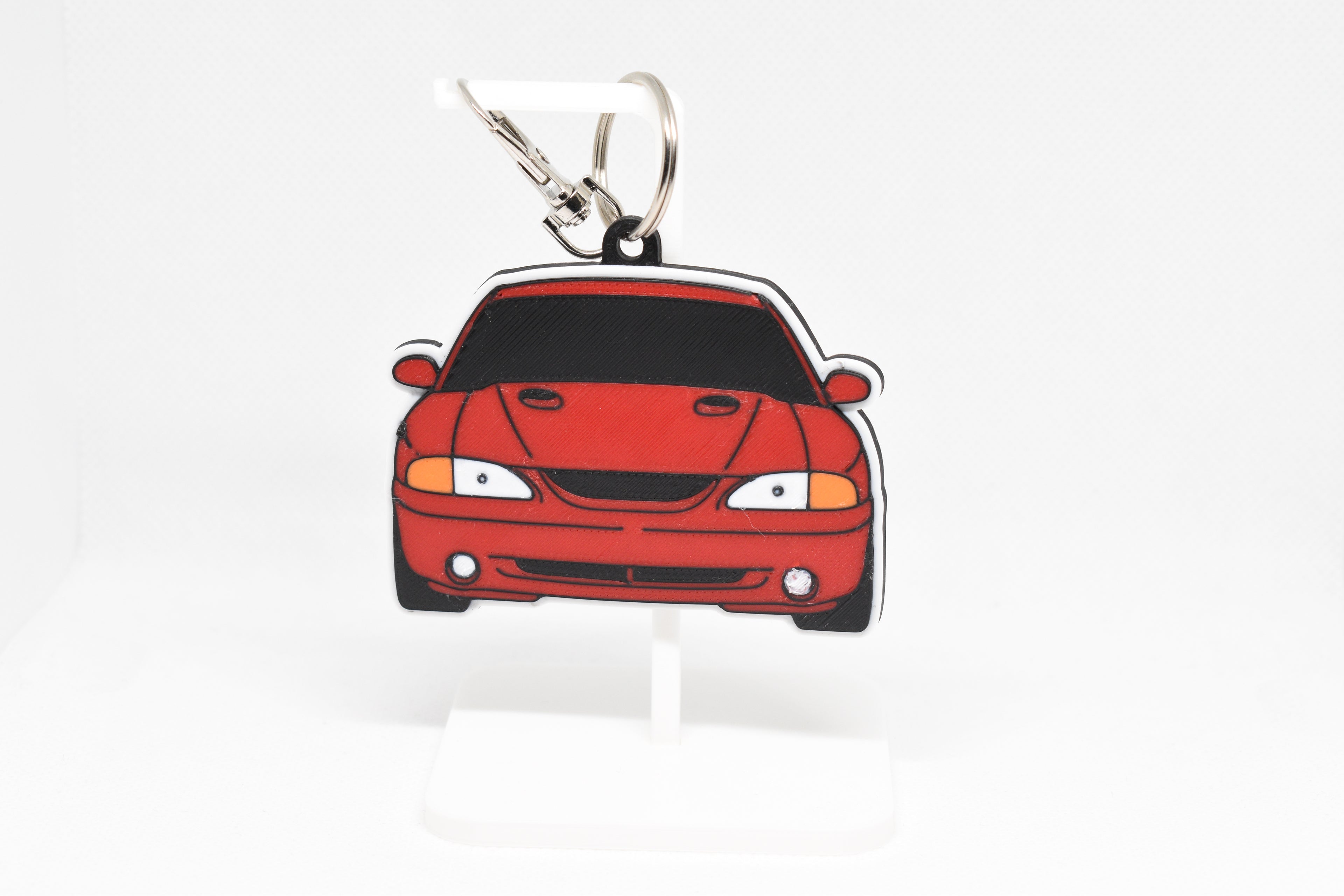 Pocket Motors Mustang Cobra SN95 keychain displayed on a white stand with metal ring and clip.