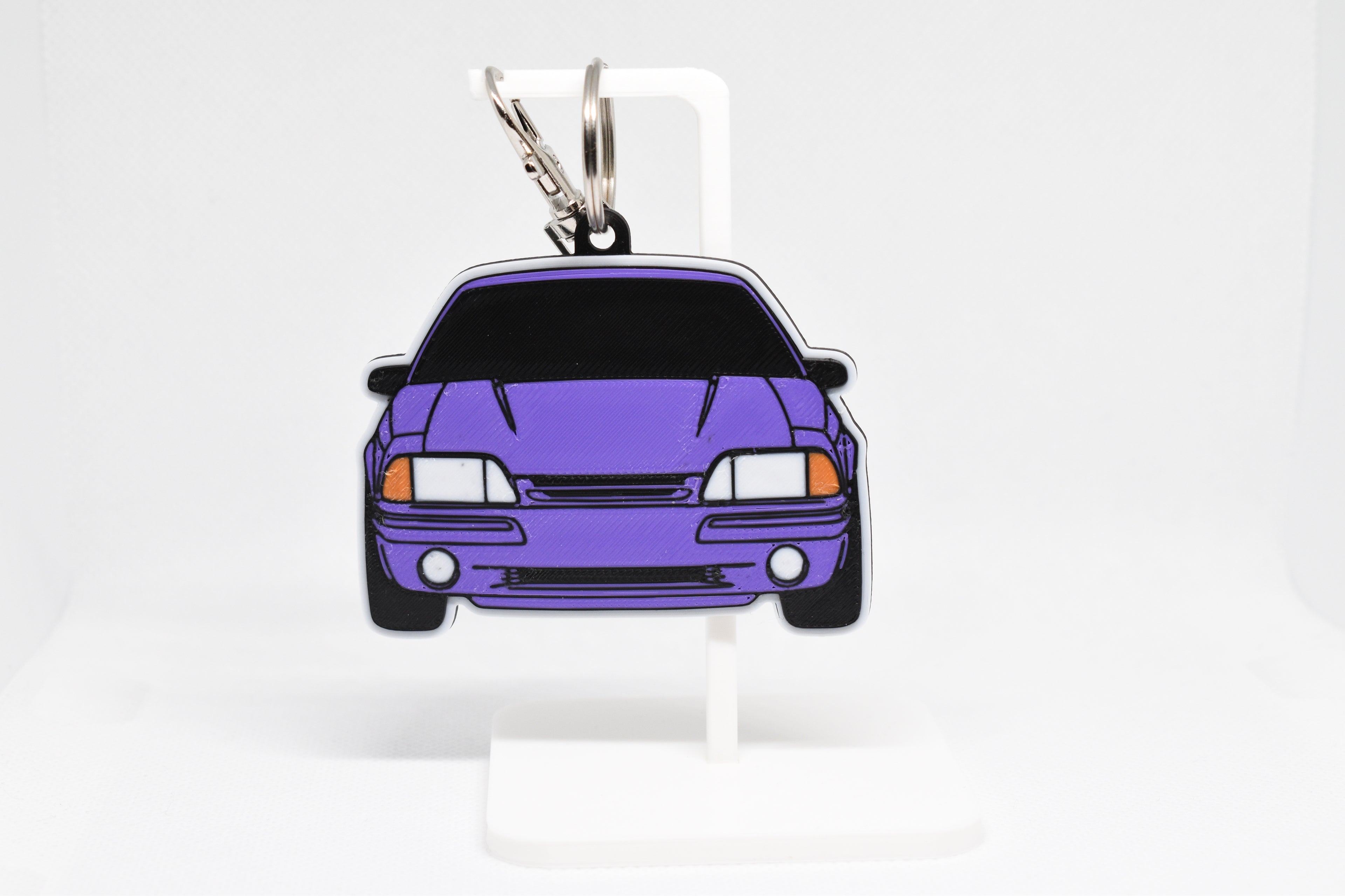 Pocket Motors Mustang Foxbody keychain displayed on a white stand with metal ring and clip.