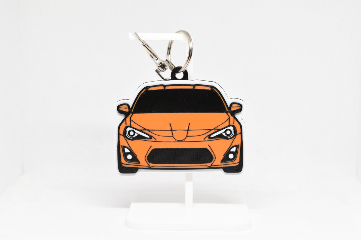 Layerplay Pocket Motors Toyota GT86 3D printed keychain displayed on a white stand.