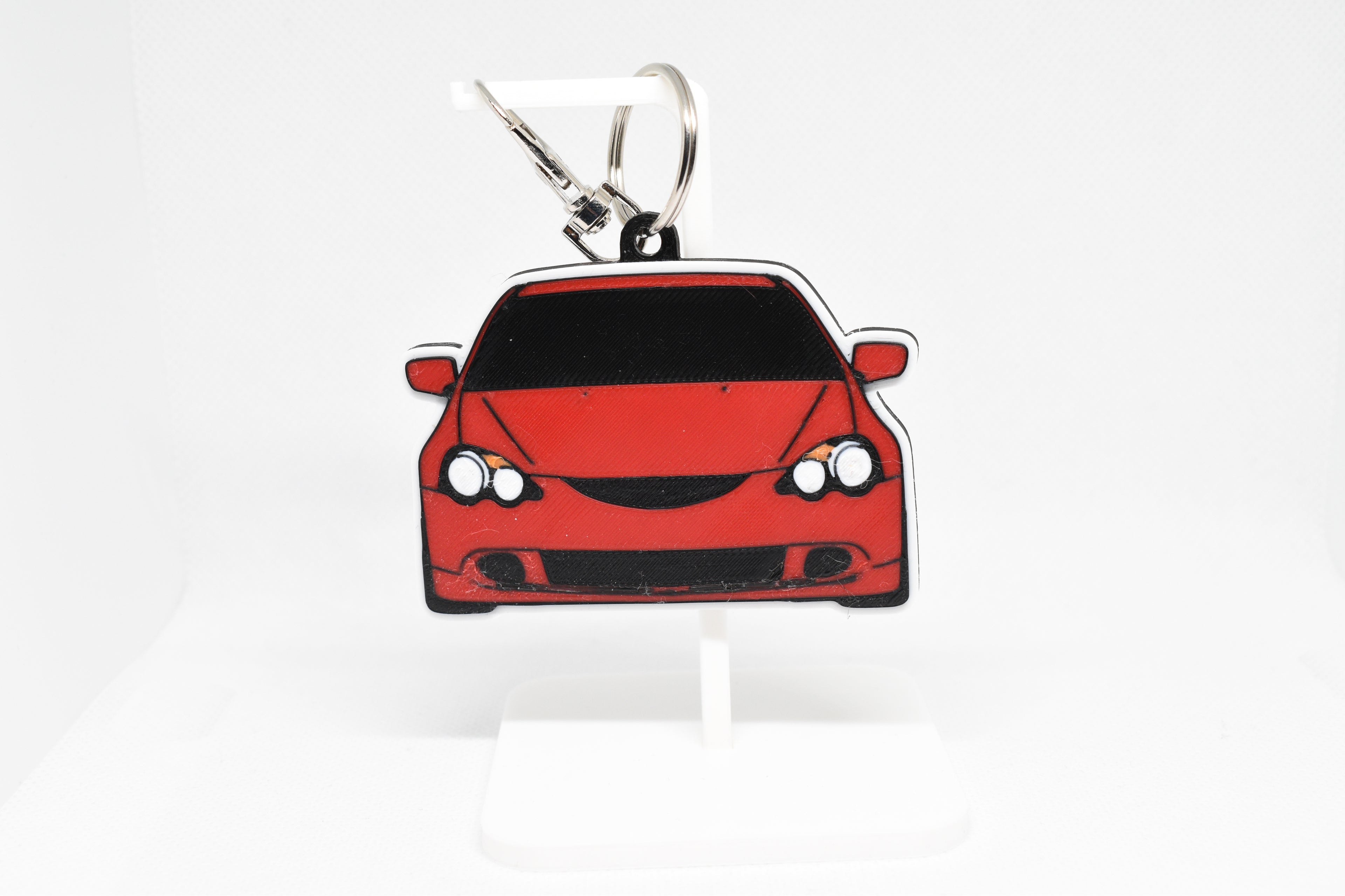 Red RSX keychain displayed on a white stand with metal ring and clip.