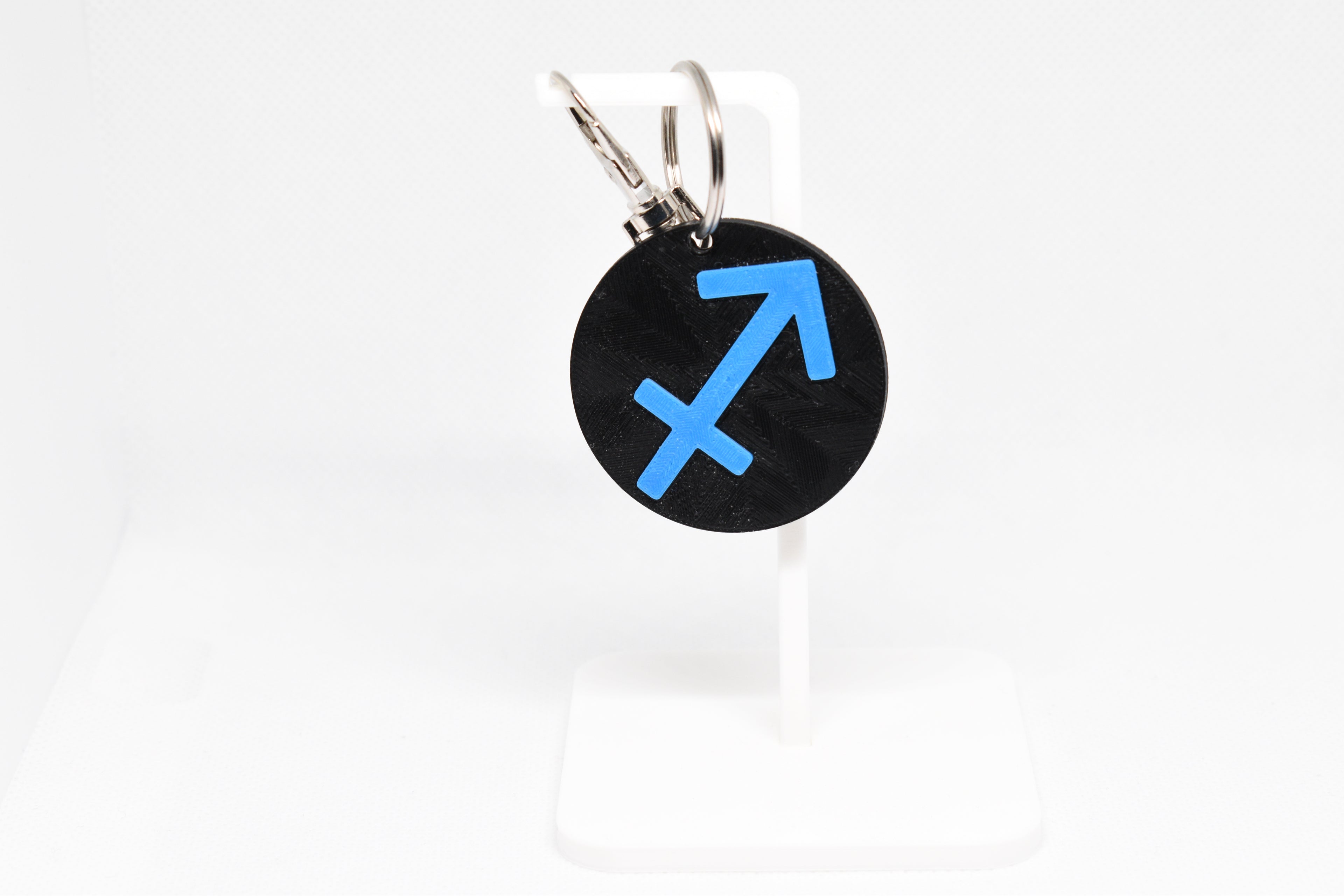 Sagittarius zodiac keychain with blue symbol displayed on a white stand with metal ring and clip.