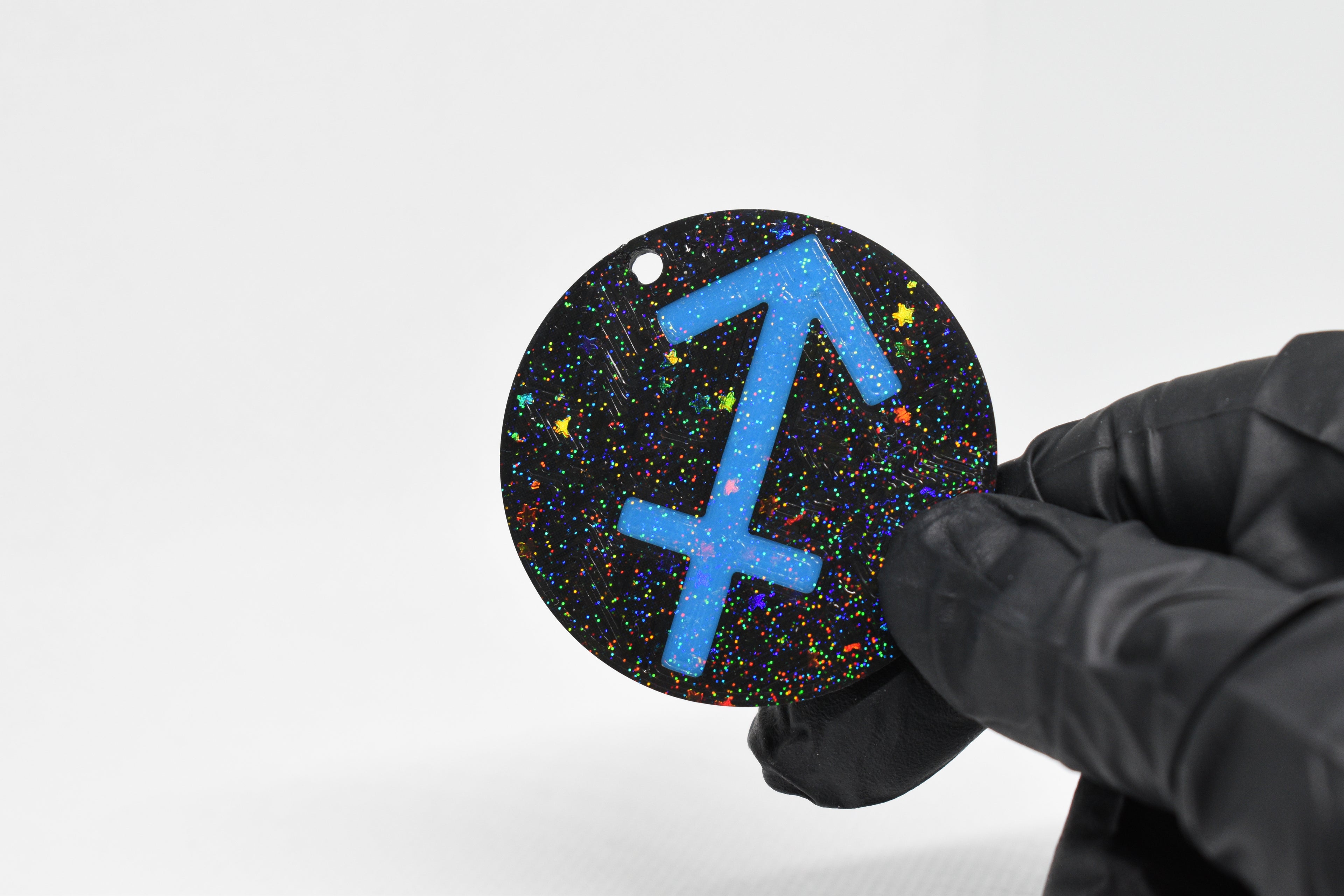 Sagittarius zodiac keychain with blue symbol and glitter‑black cosmic background held in a gloved hand.