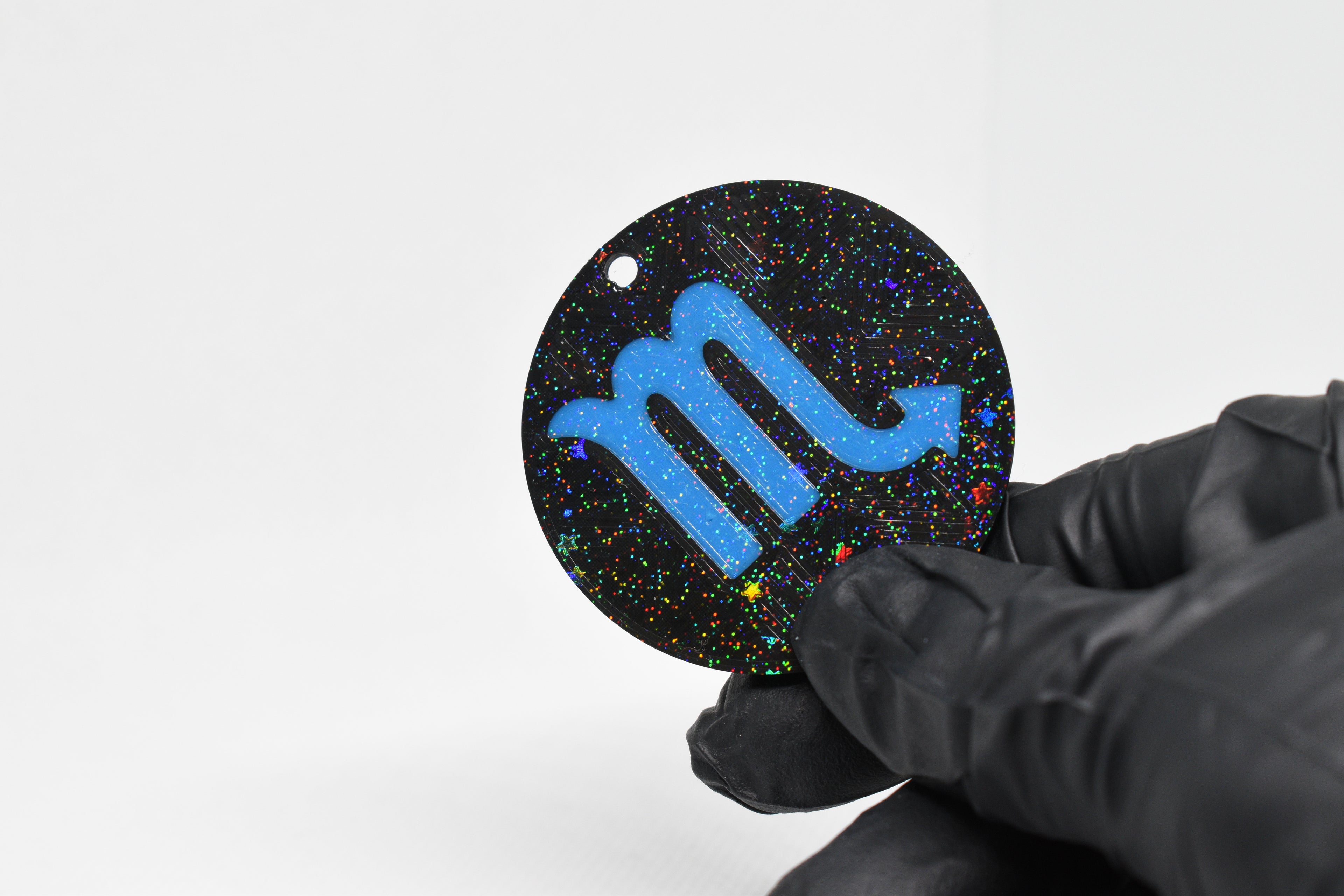 Scorpio zodiac keychain with blue symbol and glitter‑black cosmic background held in a gloved hand.