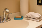 Cyan DominoBase soap dish holding a bar soap on a bathroom vanity counter near chrome faucet by LayerPlay Solara