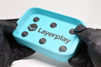 Hands in black gloves holding 3D printed cyan DominoBase soap dish with black raised nubs by LayerPlay Solara