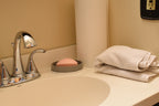 3D printed grey ElevateFlow soap dish holding a pink soap bar on a white bathroom vanity counter by LayerPlay Solara