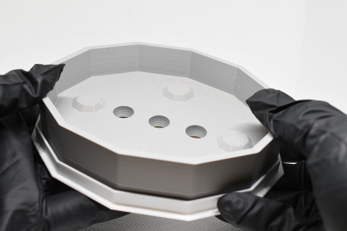Hands in black gloves holding a 3D printed grey and white geometric octagonal ElevateFlow soap dish by LayerPlay Solara