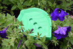 Green leaf pattern 3D printed self-draining soap holder nestled in garden foliage with purple flowers by LayerPlay Solara