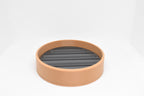Low front studio view showing textured tan outer rim and black slotted grate insert of soap dish by LayerPlay Solara
