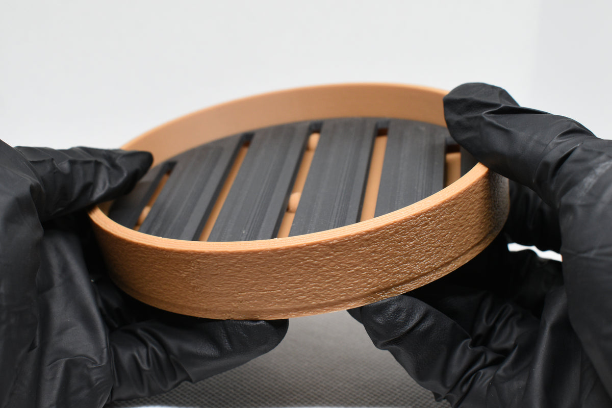 Hands in black gloves holding 3D printed two tone tan and black self-draining soap dish by LayerPlay Solara