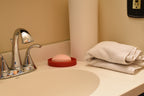 3D printed red TriLift soap dish holding a pink bar of soap on a bathroom vanity counter next to a chrome faucet by LayerPlay Solara