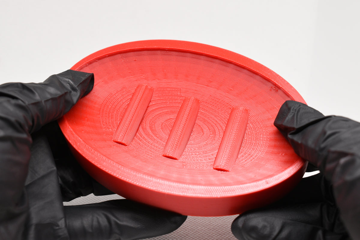 Close up held in hands showing textured surface and triple raised bar ridges of 3D printed red soap holder by LayerPlay Solara