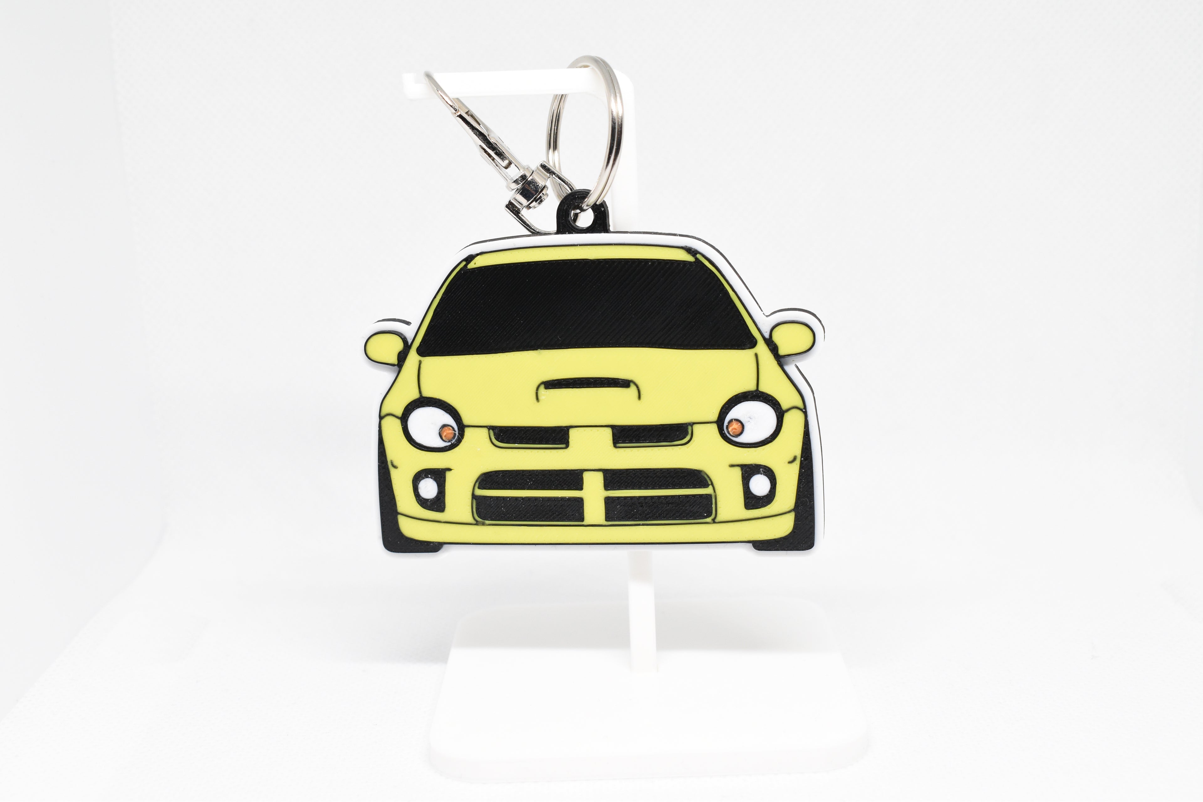 Yellow Neon SRT‑4 keychain displayed on a white stand with metal ring and clip.