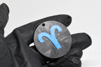 Hand in black glove holding 3D printed blue aries zodiac symbol keychain front view detail by LayerPlay
