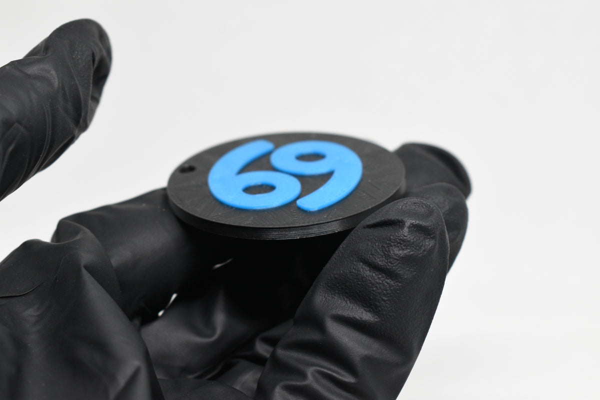 Side angle view showing raised 3D blue cancer sign detail and thickness on black disc keychain by LayerPlay