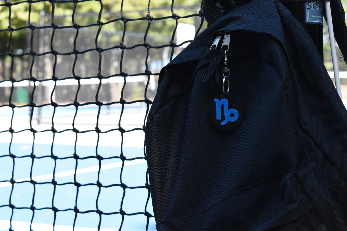 3D printed capricorn zodiac keychain clipped to a black backpack zipper outdoors near a tennis court by LayerPlay
