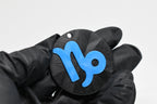 Hand in black glove holding 3D printed blue capricorn zodiac symbol keychain front view detail by LayerPlay