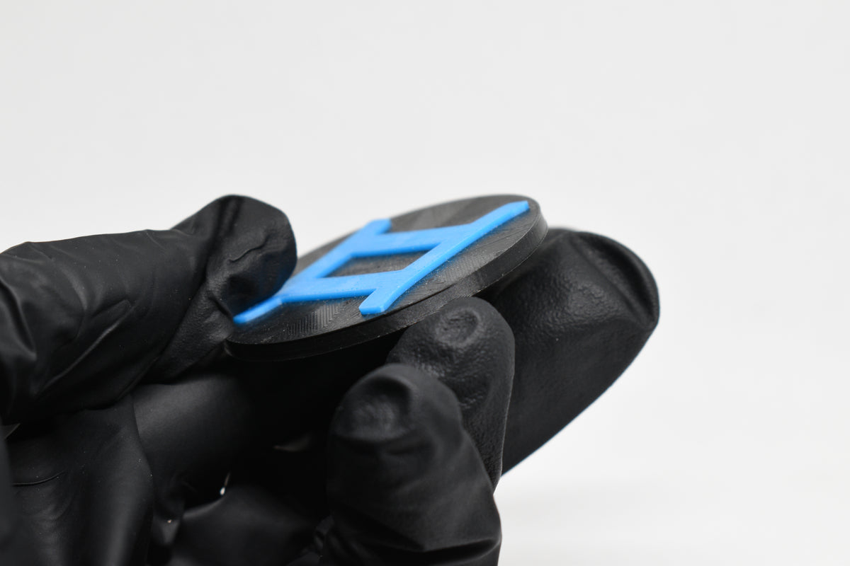 Side angle view showing raised 3D blue gemini sign detail and thickness on black disc keychain by LayerPlay