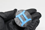 Hand in black glove holding 3D printed blue gemini zodiac symbol keychain front view detail by LayerPlay