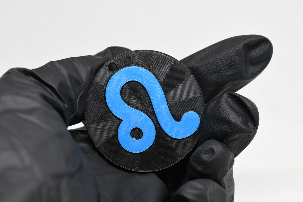 Hand in black glove holding 3D printed blue leo zodiac symbol keychain front view detail by LayerPlay