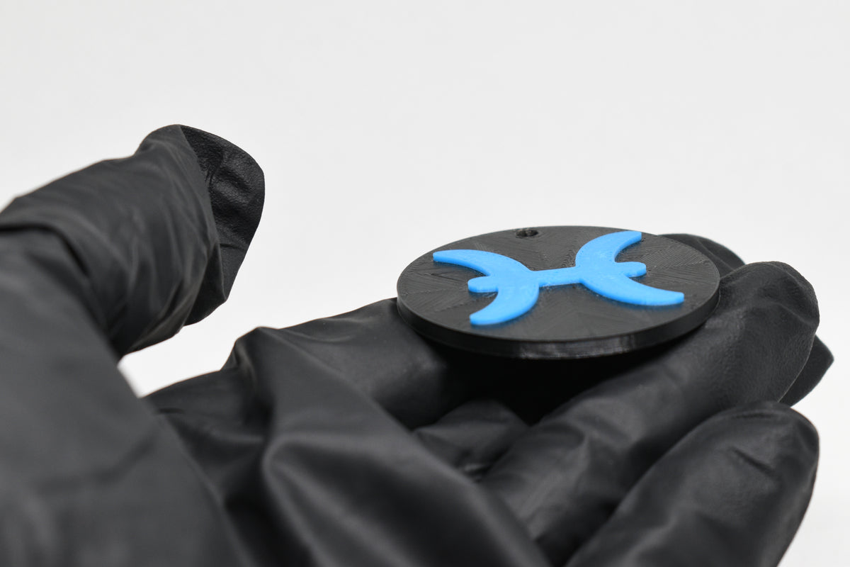 Side angle view showing raised 3D blue pisces sign detail and thickness on black disc keychain by LayerPlay