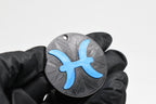 Hand in black glove holding 3D printed blue pisces zodiac symbol keychain front view detail by LayerPlay