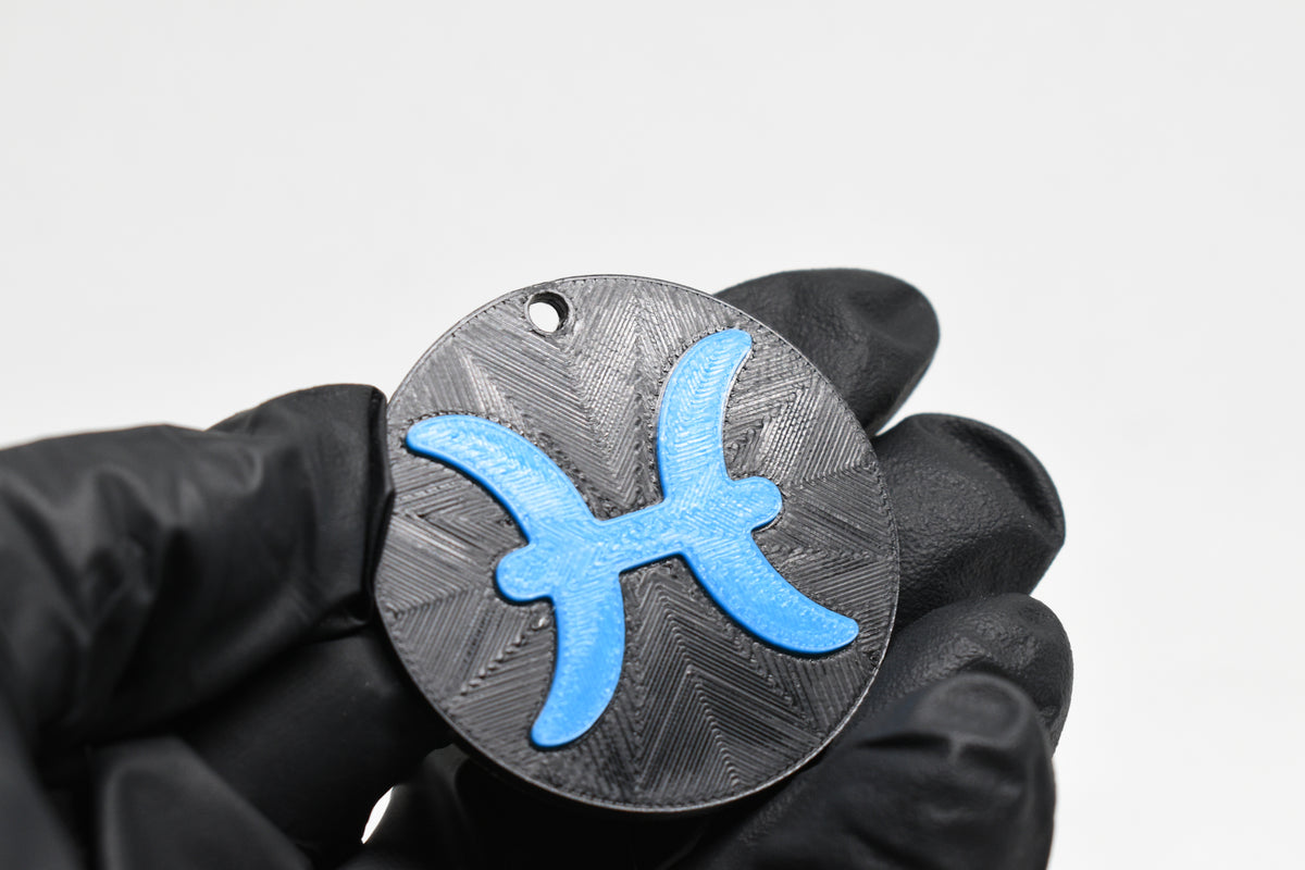 Hand in black glove holding 3D printed blue pisces zodiac symbol keychain front view detail by LayerPlay