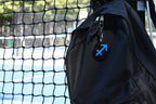 3D printed sagittarius zodiac keychain clipped to a black backpack zipper outdoors near a tennis court by LayerPlay