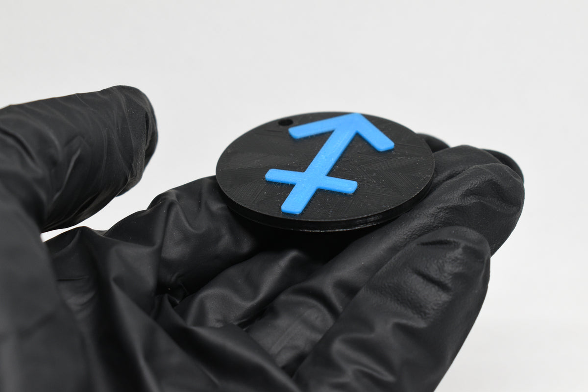 Side angle view showing raised 3D blue sagittarius sign detail and thickness on black disc keychain by LayerPlay