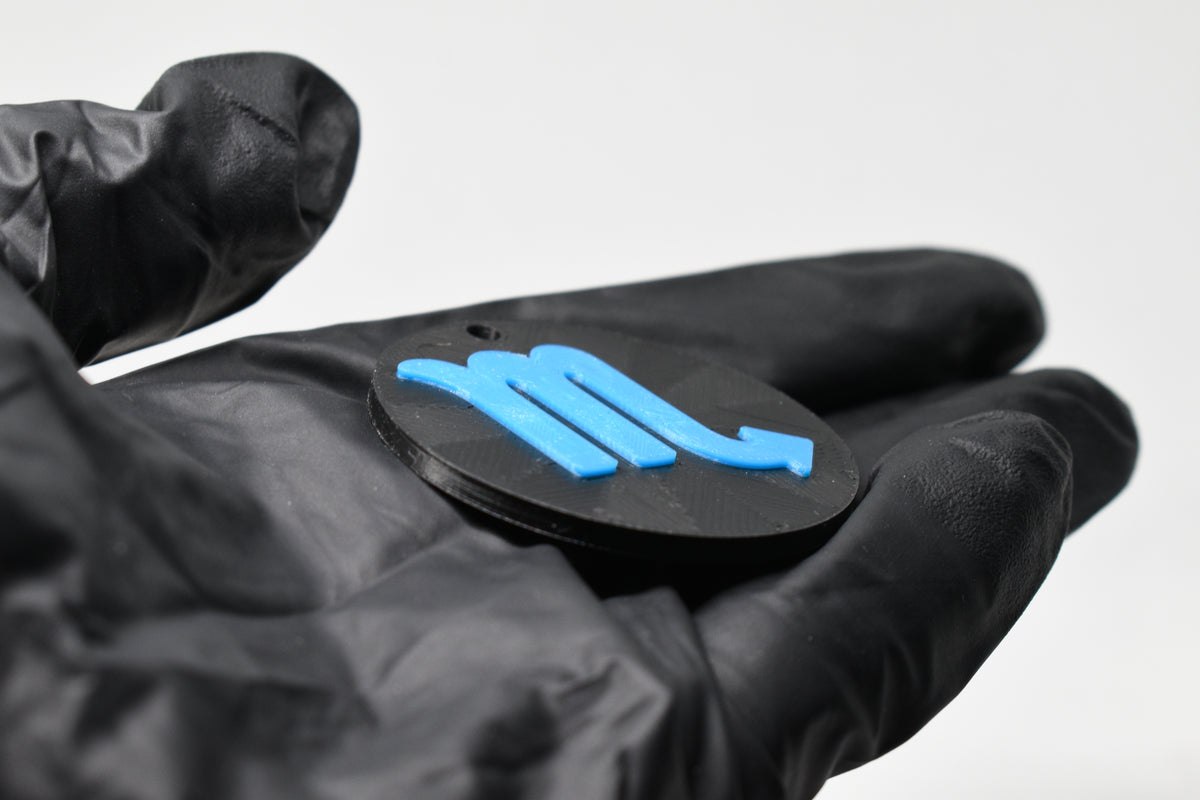 Side angle view showing raised 3D blue scorpio sign detail and thickness on black disc keychain by LayerPlay