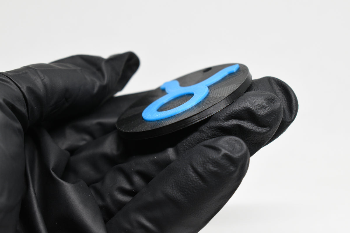 Side angle view showing raised 3D blue taurus sign detail and thickness on black disc keychain by LayerPlay