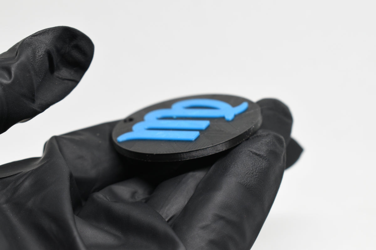Side angle view showing raised 3D blue virgo sign detail and thickness on black disc keychain by LayerPlay