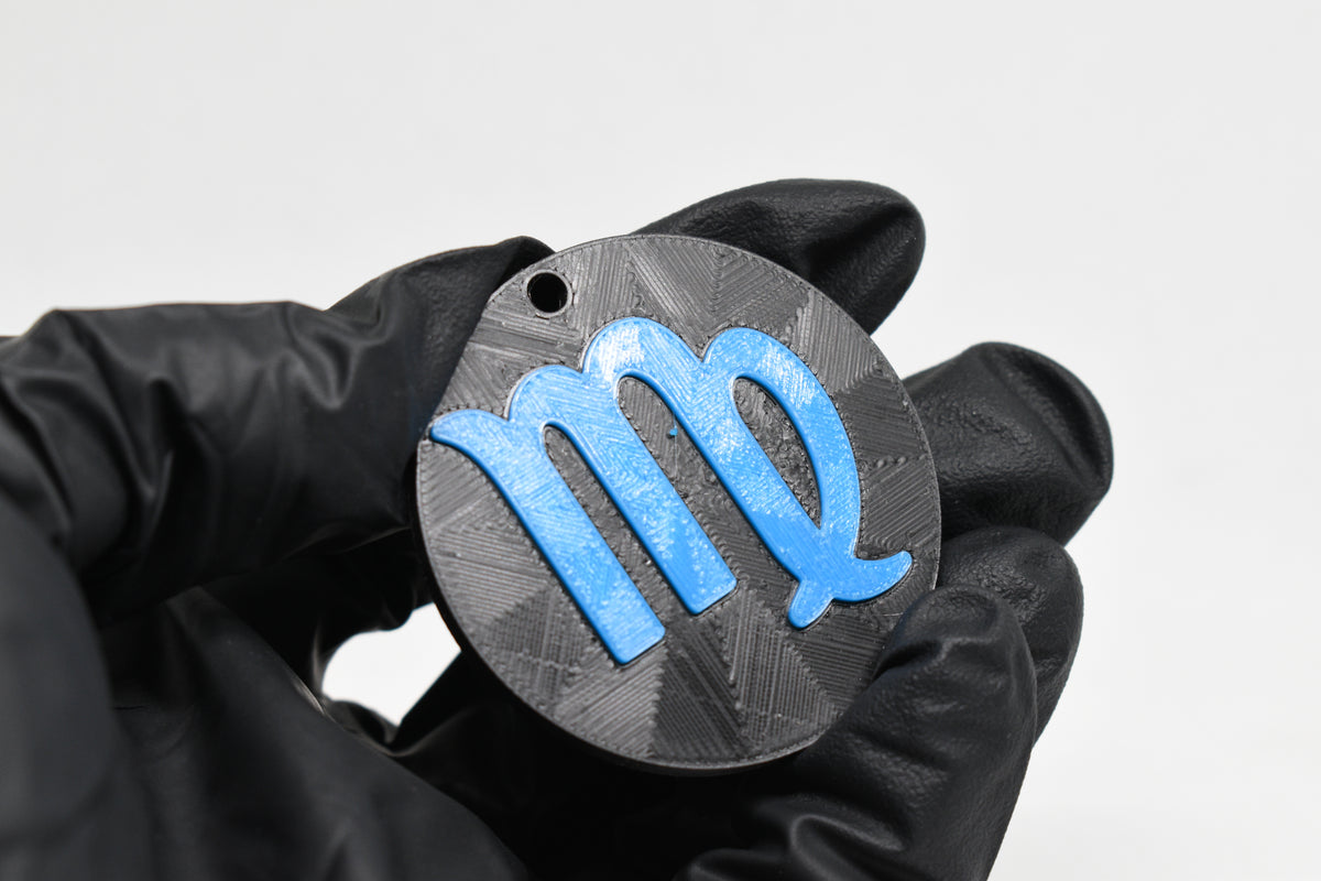 Hand in black glove holding 3D printed blue virgo zodiac symbol keychain front view detail by LayerPlay